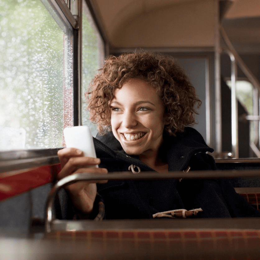 A woman is smiling while holding her phone.
